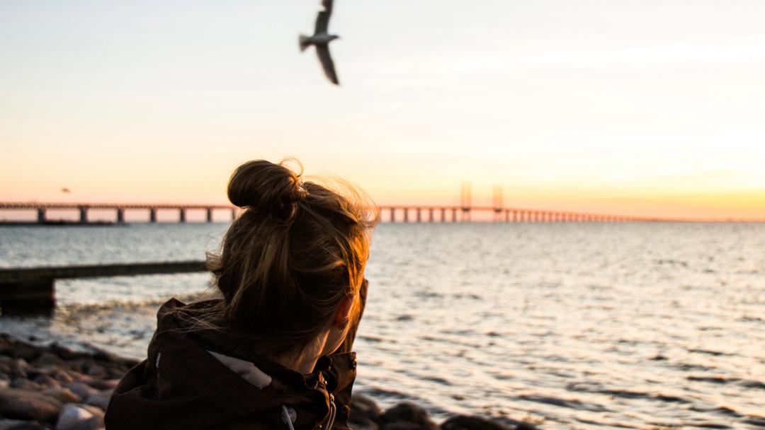 Kvinna framför Öresundsbron i solnedgången.