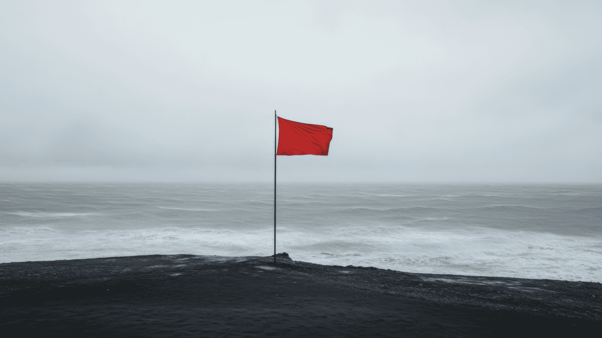 Röd flagga på klippa framför stormigt hav.